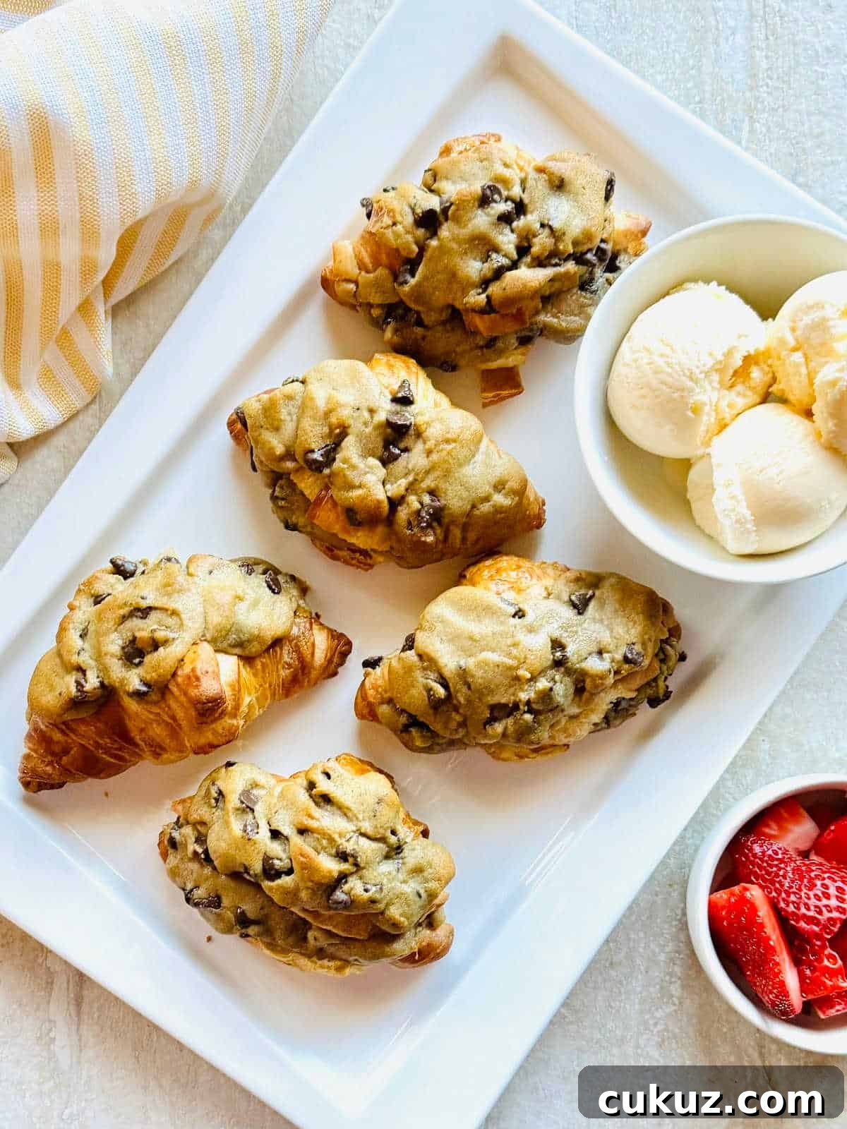 viral tiktok crookie croissant stuffed with cookie sitting next to a bowl of ice cream and strawberries.