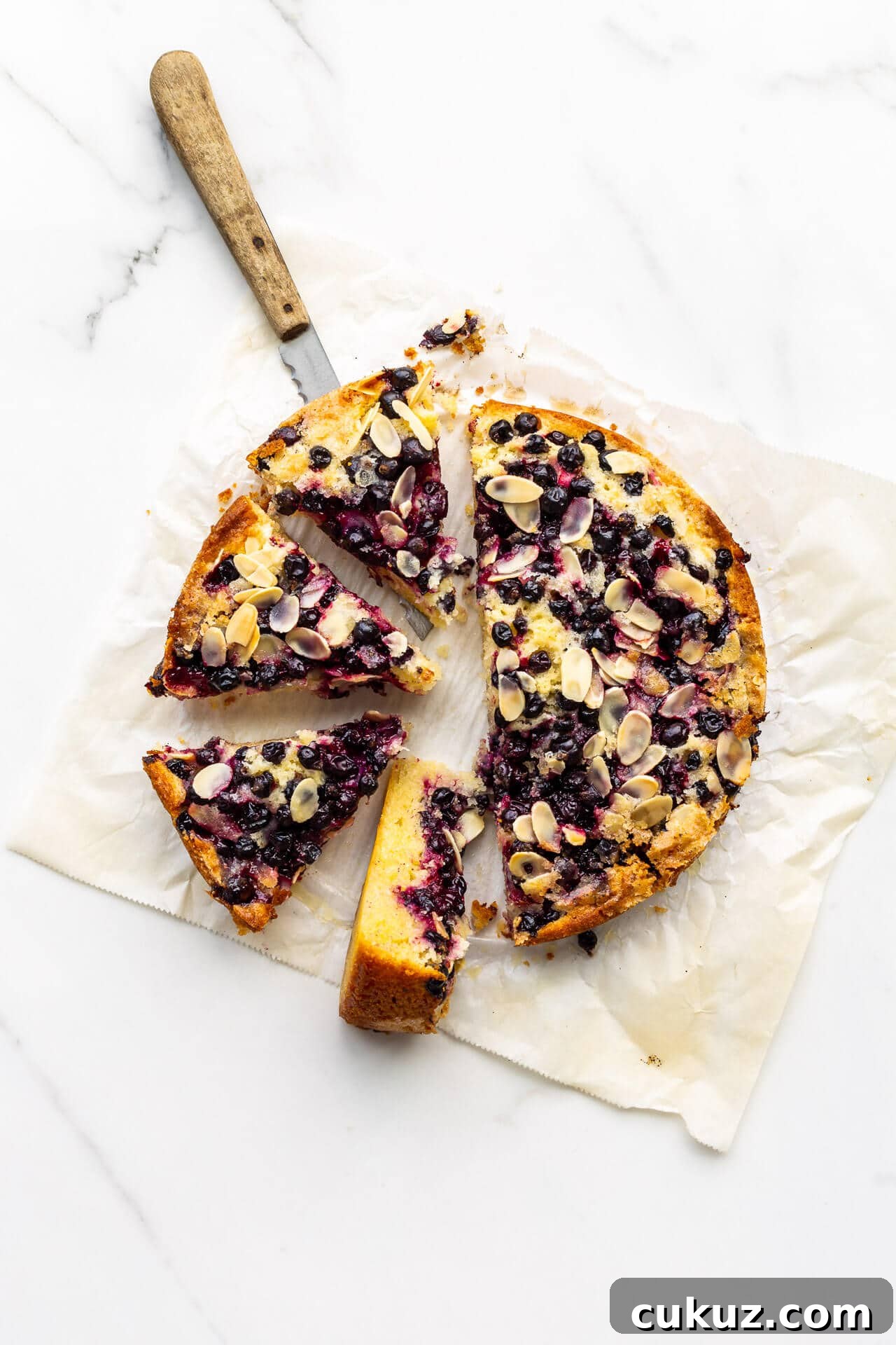 Sliced black currant cake on parchment paper with a wood-handled knife to serve