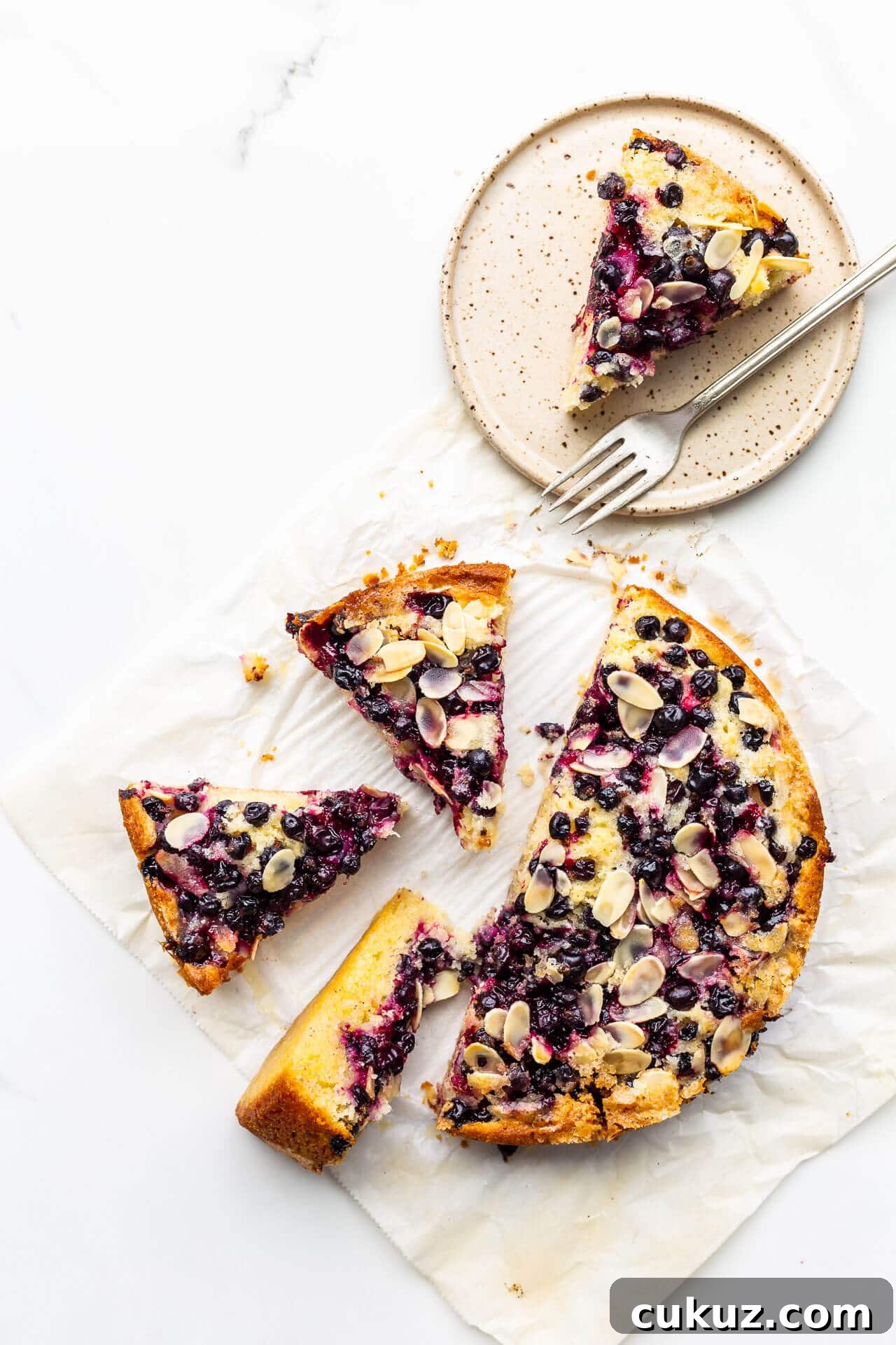 Black currant cake sliced into pieces with one on a speckled ceramic plate with a fork