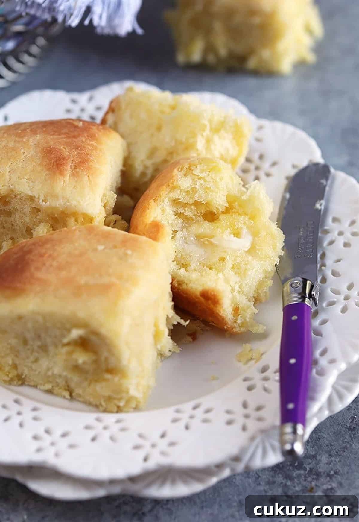 Dinner rolls on a white plate with a purple spreader with butter.