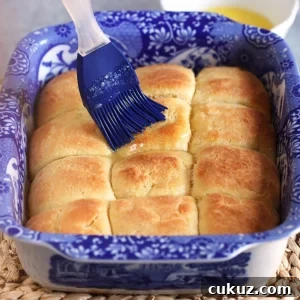 Dinner rolls in a baking dish after baking with a blue brush basting with butter.
