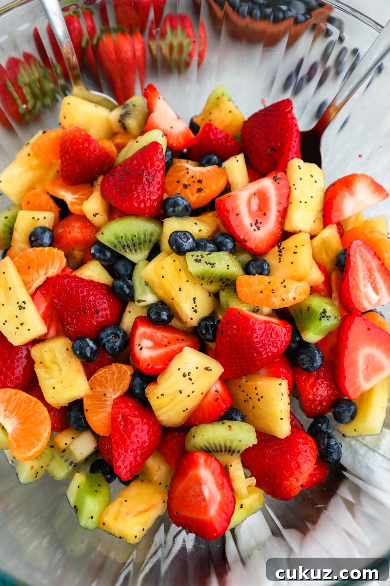 A large clear mixing bowl filled with fresh fruit salad sitting next to fresh strawberries and a bowl of blueberries