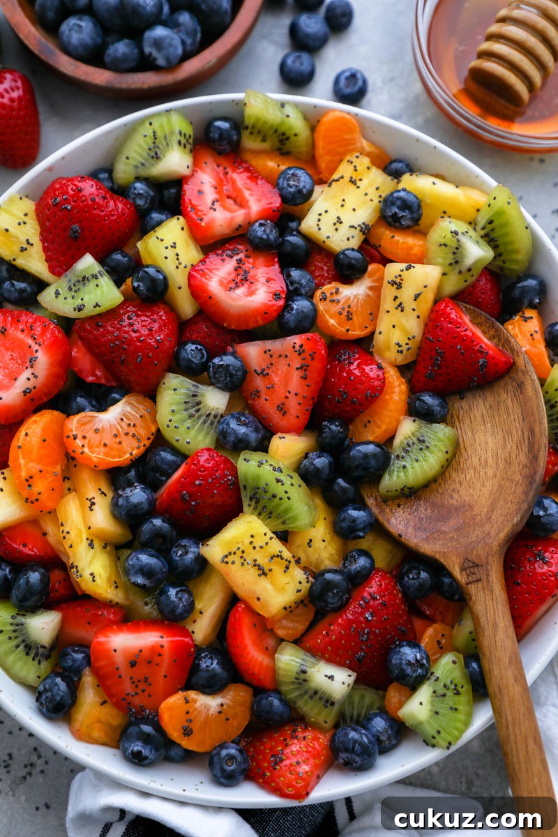 A wooden spoon digging into a large bowl of fresh fruit salad