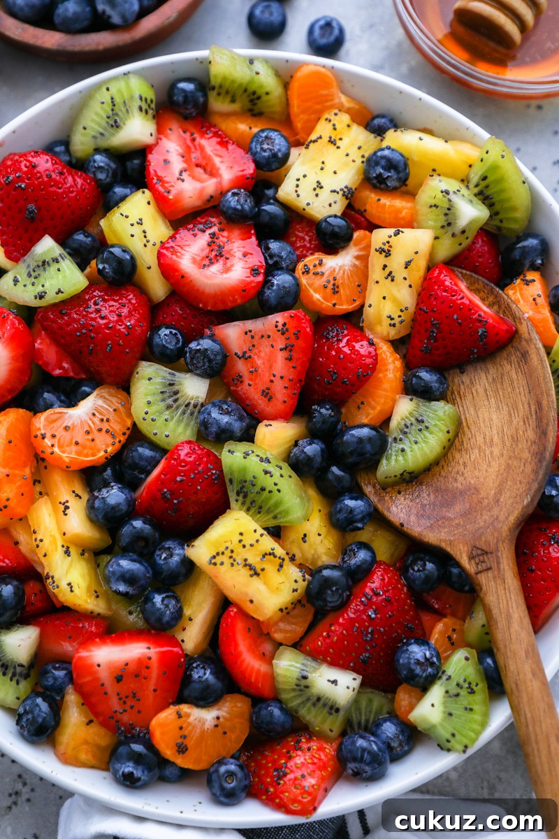 A large serving bowl filled with fresh fruit salad tossed in a honey-lime dressing