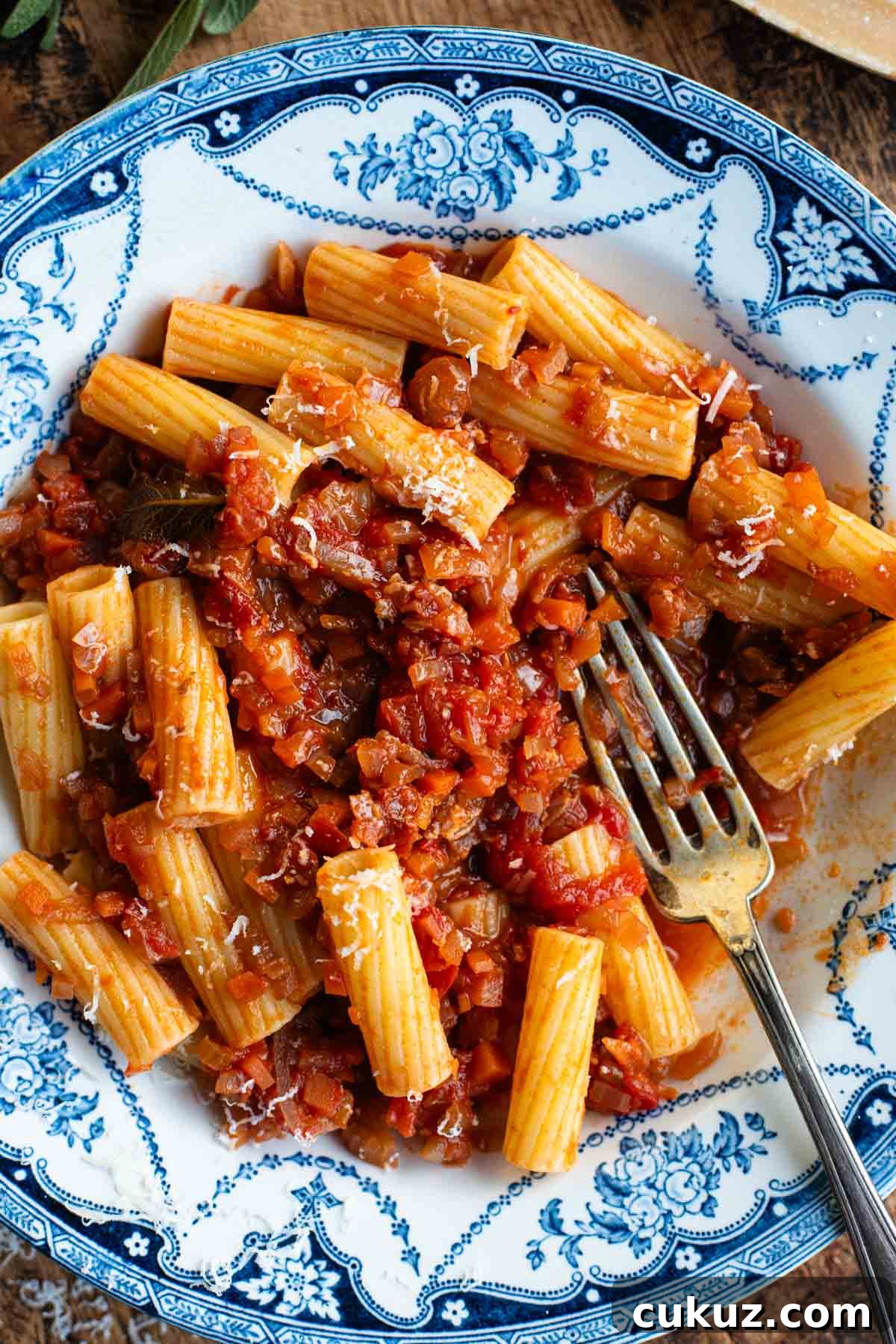 An overhead shot of rigatoni pasta with a vegetable sauce in a blue and white bowl.