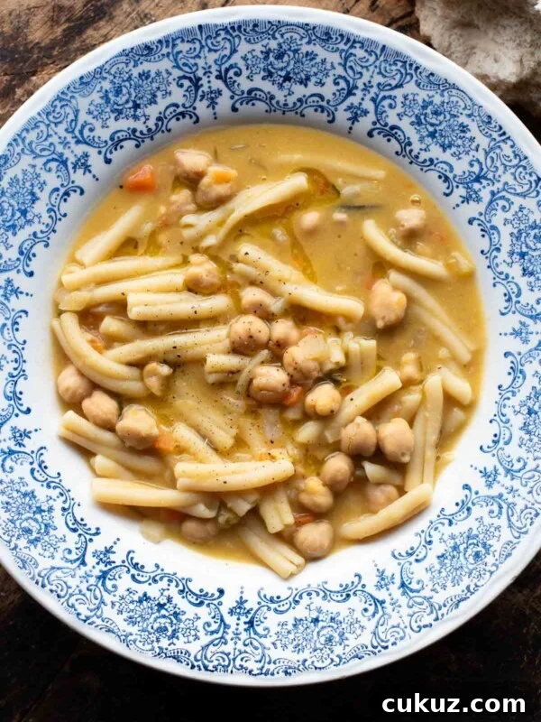 An overhead shot of pasta e ceci (psta and chickpeas) in a blue bowl on a wooden surface.