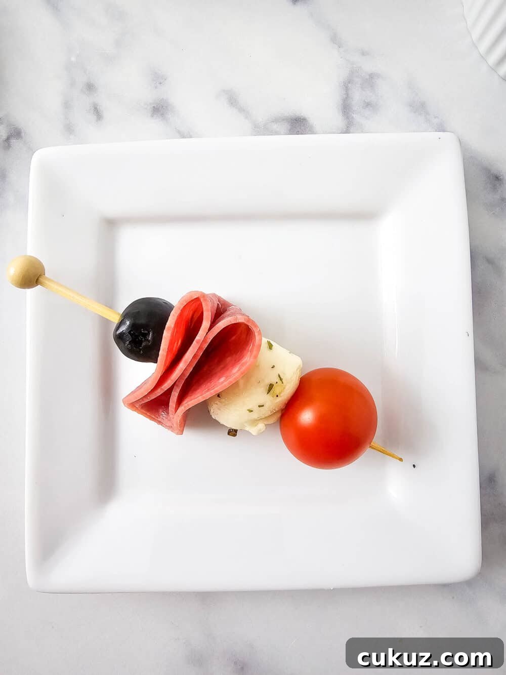 olive, salami, mozzarella ball, and cherry tomato on a skewer