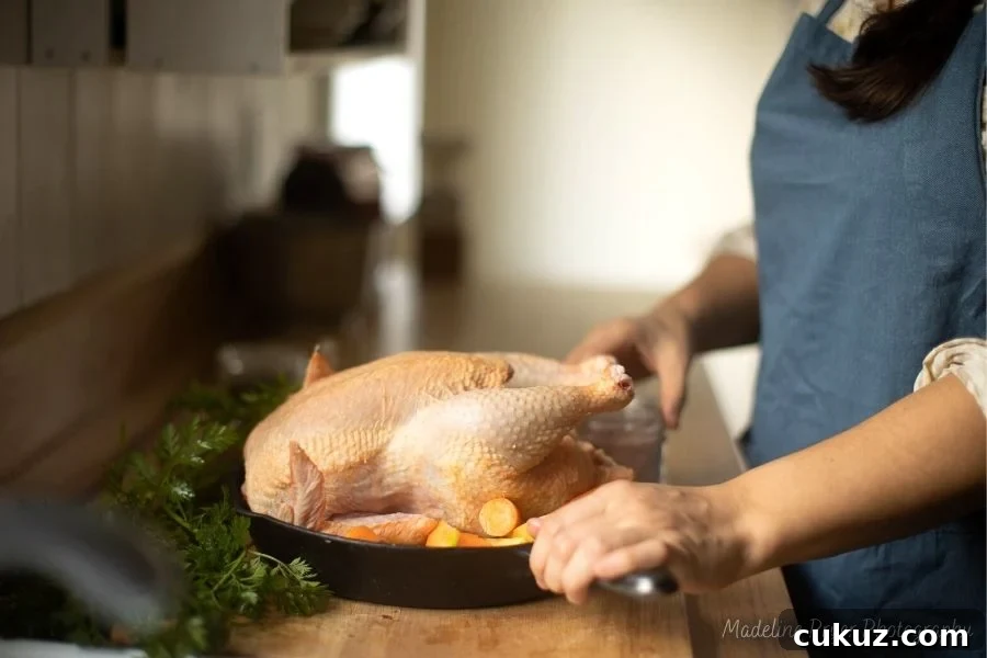 a woman at the kitchen counter in a blue apron, preparing a whole chicken for baking