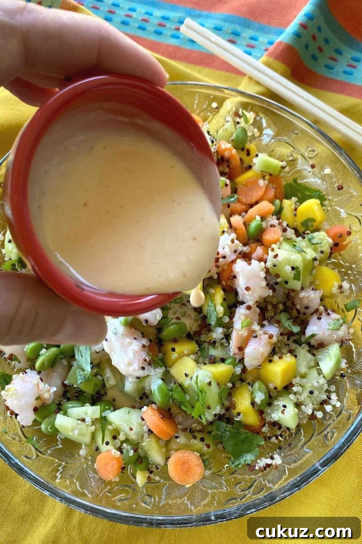 Creamy poke sauce being poured over a poke bowl with shrimp.