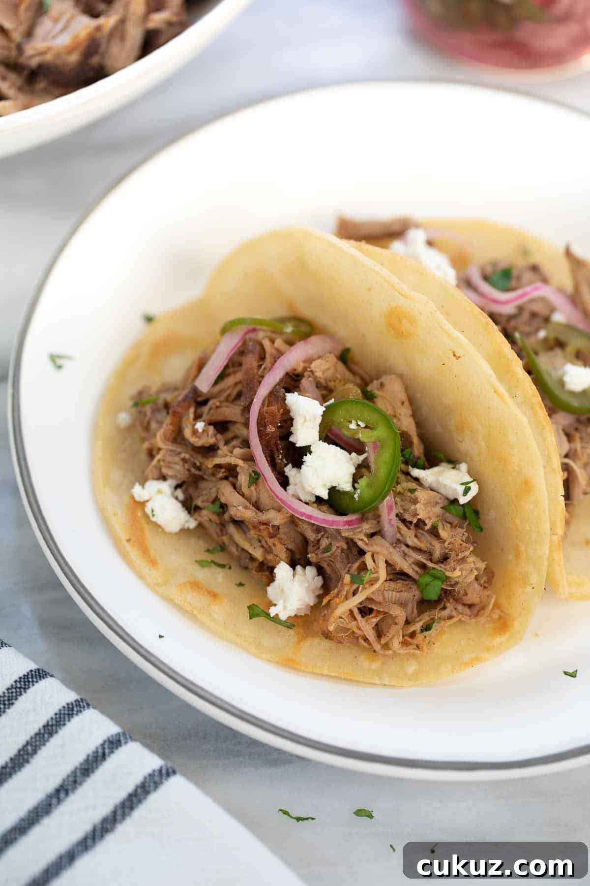 Slow-Cooker Sweet Pork Tacos Recipe for Flavorful Weeknight Meals 2 pork taco on white plate topped with pickled onions and cilantro