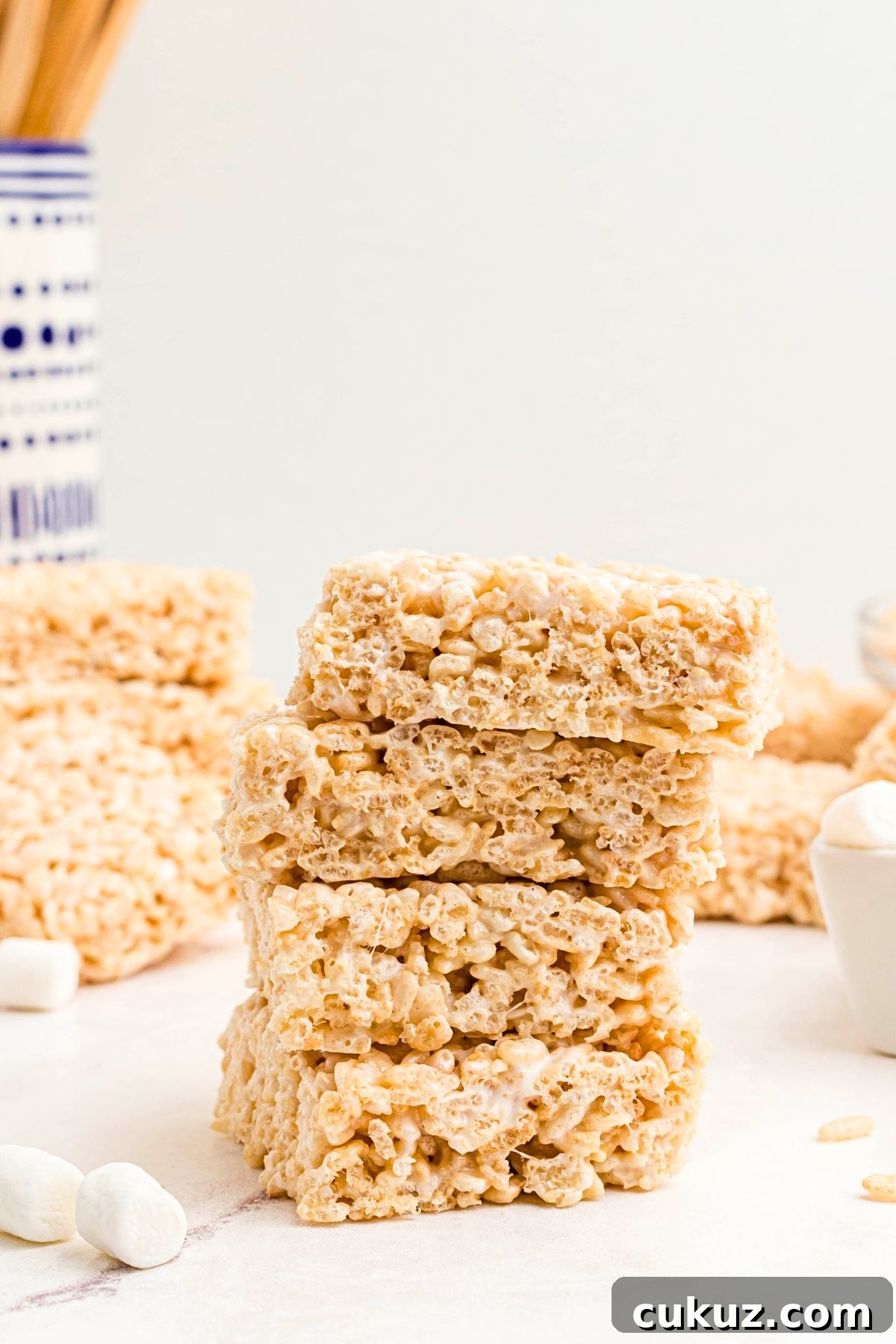 Rice krispie treats stacked on a marble table in front of other slices. 