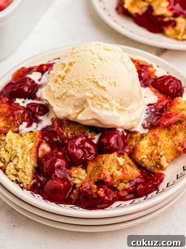 Golden crusted cherry dump cake on white plates topped with vanilla ice cream.