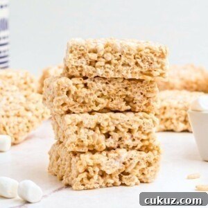 Four rice krispie treats stacked together on a white marble table with mini marshmallows on the table.