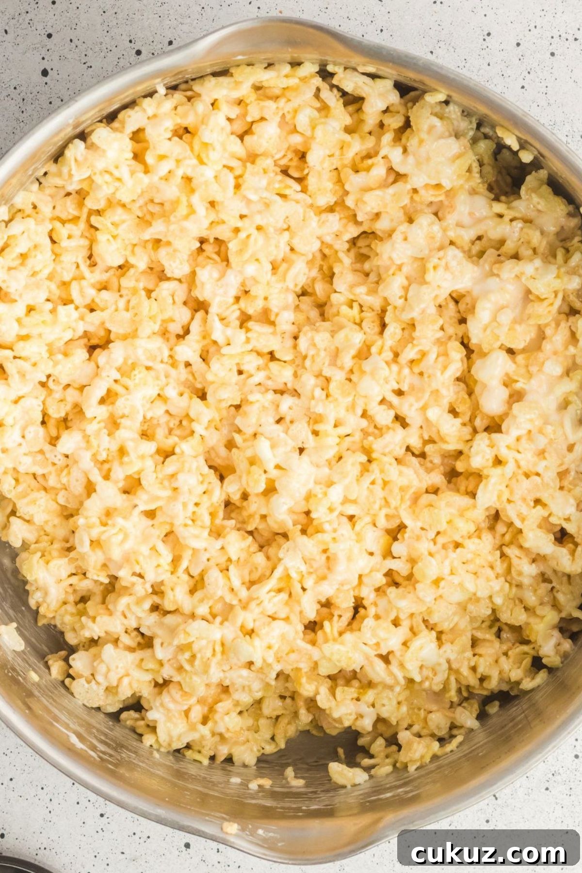 Rice cereal mixed together with melted marshmallows and melted butter in a silver pot. 