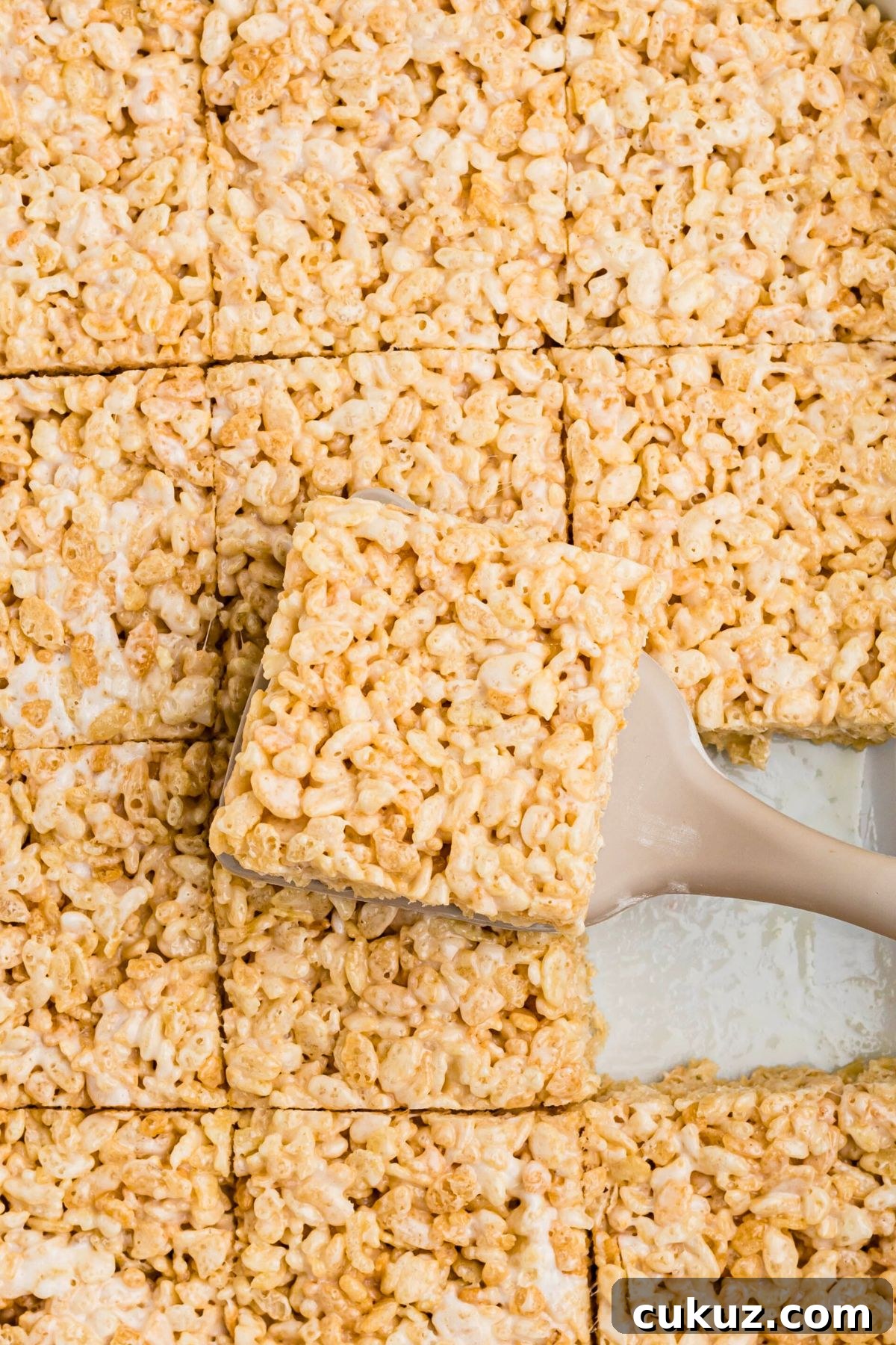Rice krispie treats cut into squares with one piece being lifted out with a spatula. 
