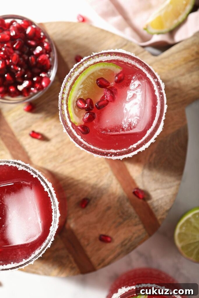 Two pomegranate margaritas on wood garnished with lime and pomegranate arils