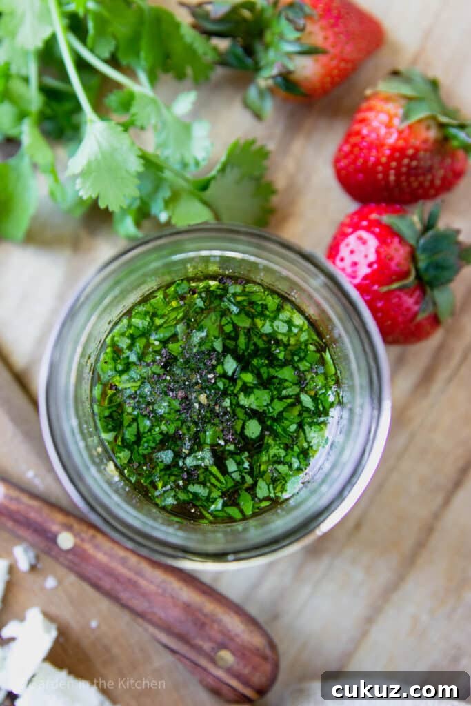 A jar of cilantro lime dressing. Fresh strawberries, cilantro and feta cheese on the table.