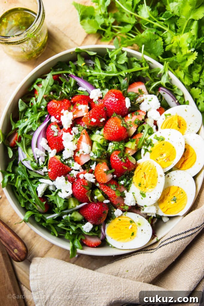 Salad in a bowl with strawberry, arugula, feta, red onions and hard boiled eggs.