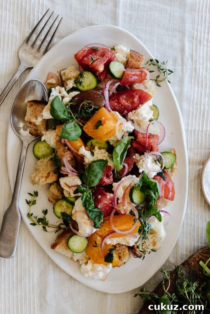 Rustic Panzanella Salad with Heirloom Tomatoes and Basil 2 panzanella salad on a white platter on a linen tablecloth with a fork and knife leaning on the platter