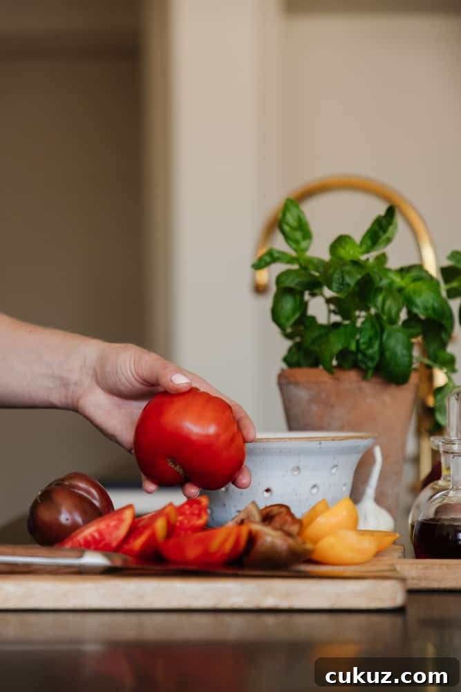 Rustic Panzanella Salad with Heirloom Tomatoes and Basil 5 hand grabbing a fresh tomato with cut tomatoes on a cutting board with fresh herbs in a vase in the background