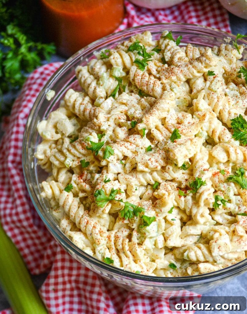 creamy macaroni salad in a glass bowl on top of a red checkered cloth napkin