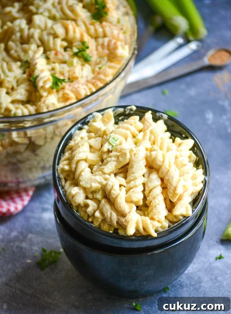 creamy macaroni salad in a glass bowl being shown served in a stack of smaller black bowls
