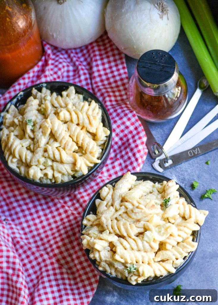 creamy cajun pasta salad shown in two black bowls on top of a red & white checkered cloth napkin