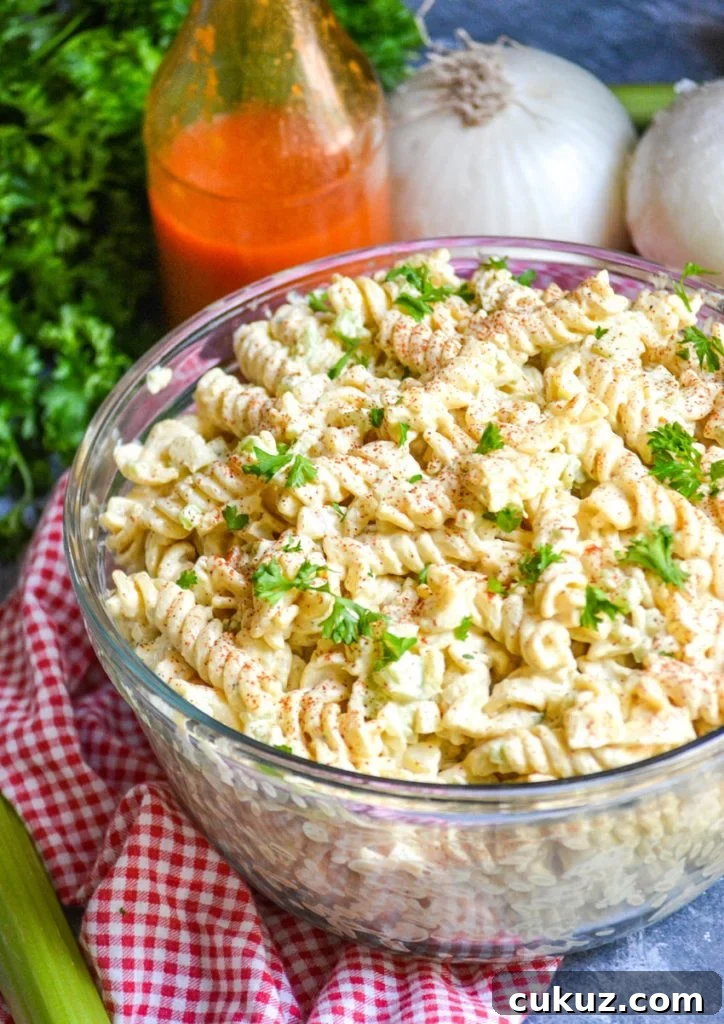 creamy macaroni salad in a glass bowl on top of a red checkered cloth napkin