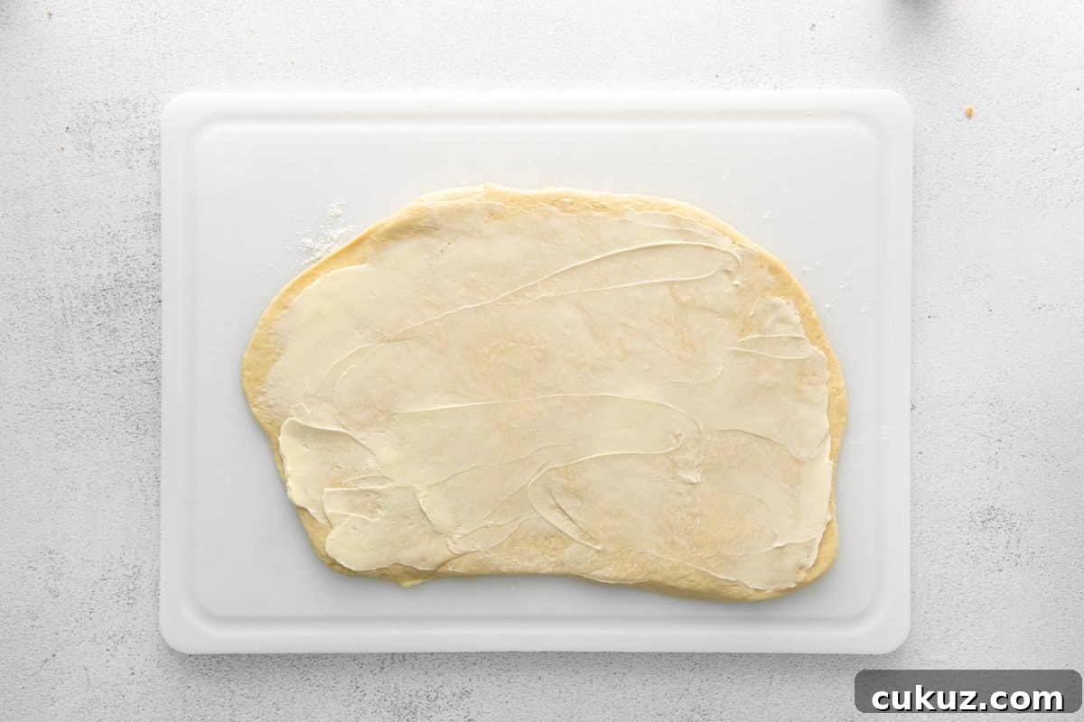 Cinnamon Roll Muffins: Soft Swirl Muffin Recipe with Cream Cheese Glaze 9 cinnamon roll muffin dough rolled out into a rectangle on a white cutting board.