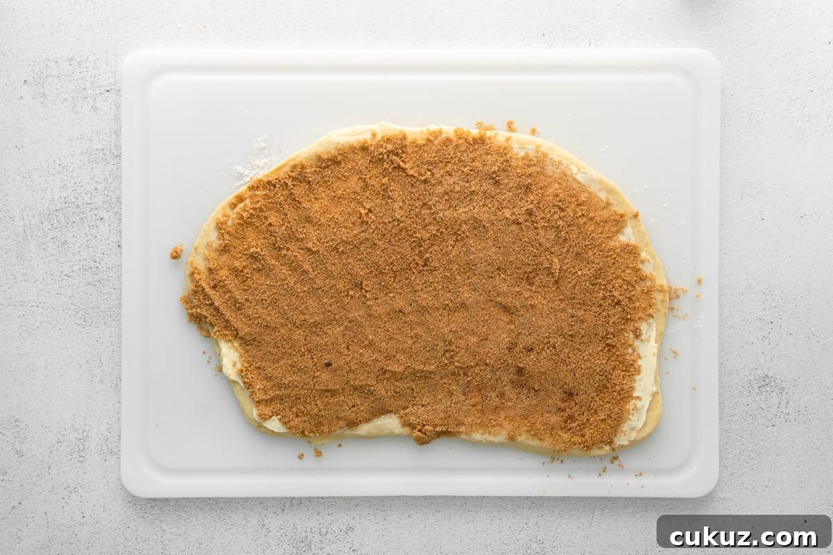 Cinnamon Roll Muffins: Soft Swirl Muffin Recipe with Cream Cheese Glaze 10 cinnamon roll filling spread over cinnamon roll dough on a white cutting board.