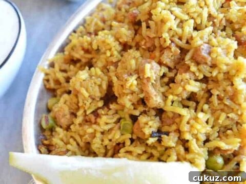A yellow platter of vegetable biryani with lemon on the side