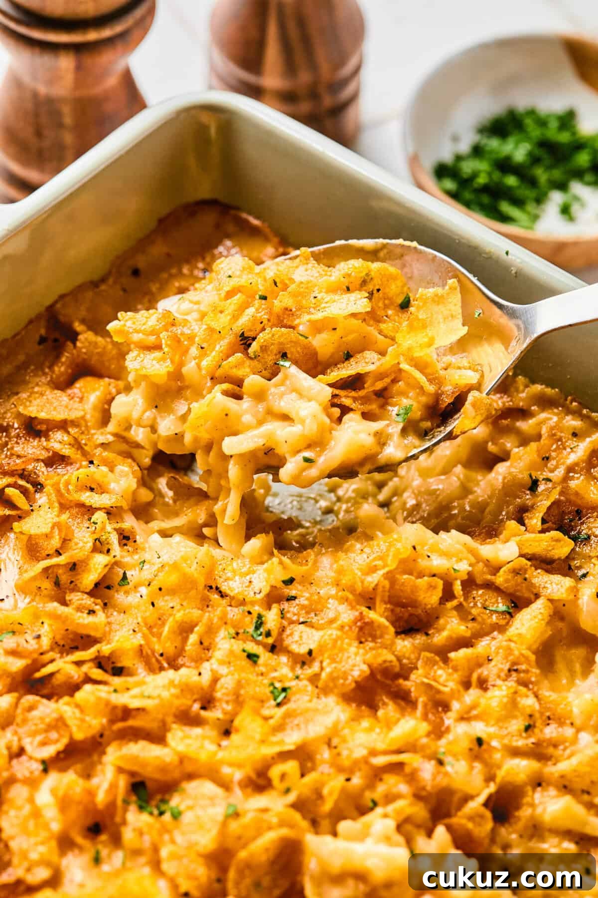 Spoon lifting out a portion of cheesy hashbrown casserole from a baking dish.