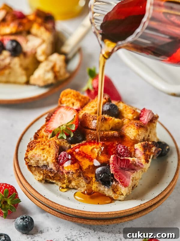 maple syrup being poured over protein french toast casserole with berries