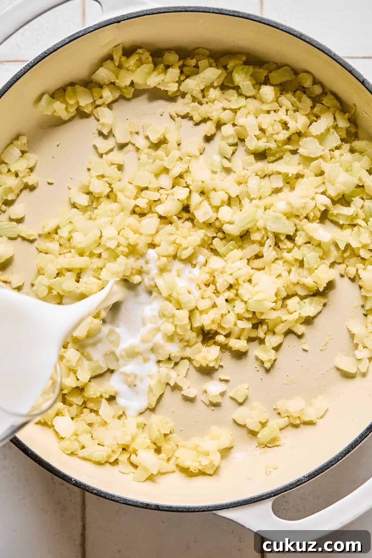 Milk being poured into the pan with sautéed onions and garlic.