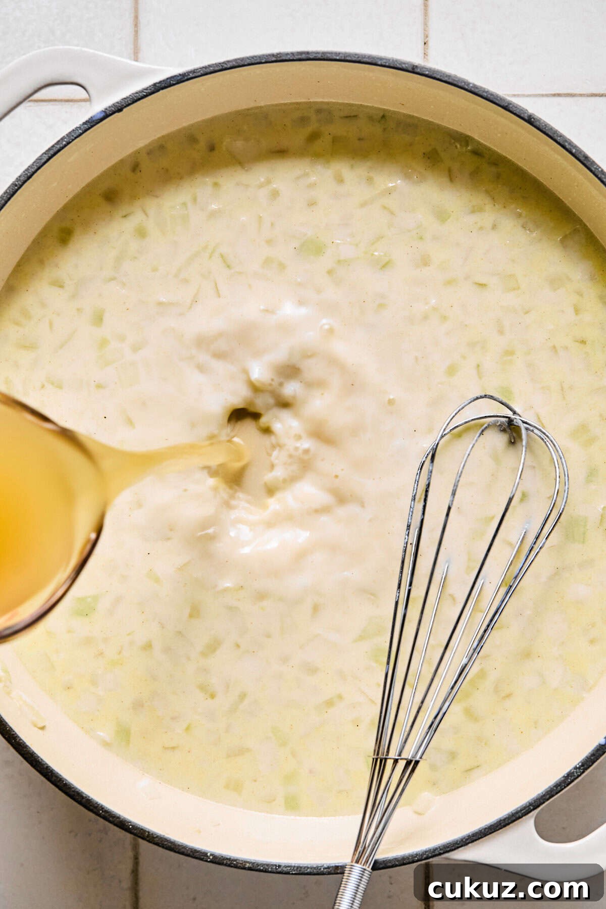 Broth being poured into the pan of milk, flour, and sautéed onions and garlic.