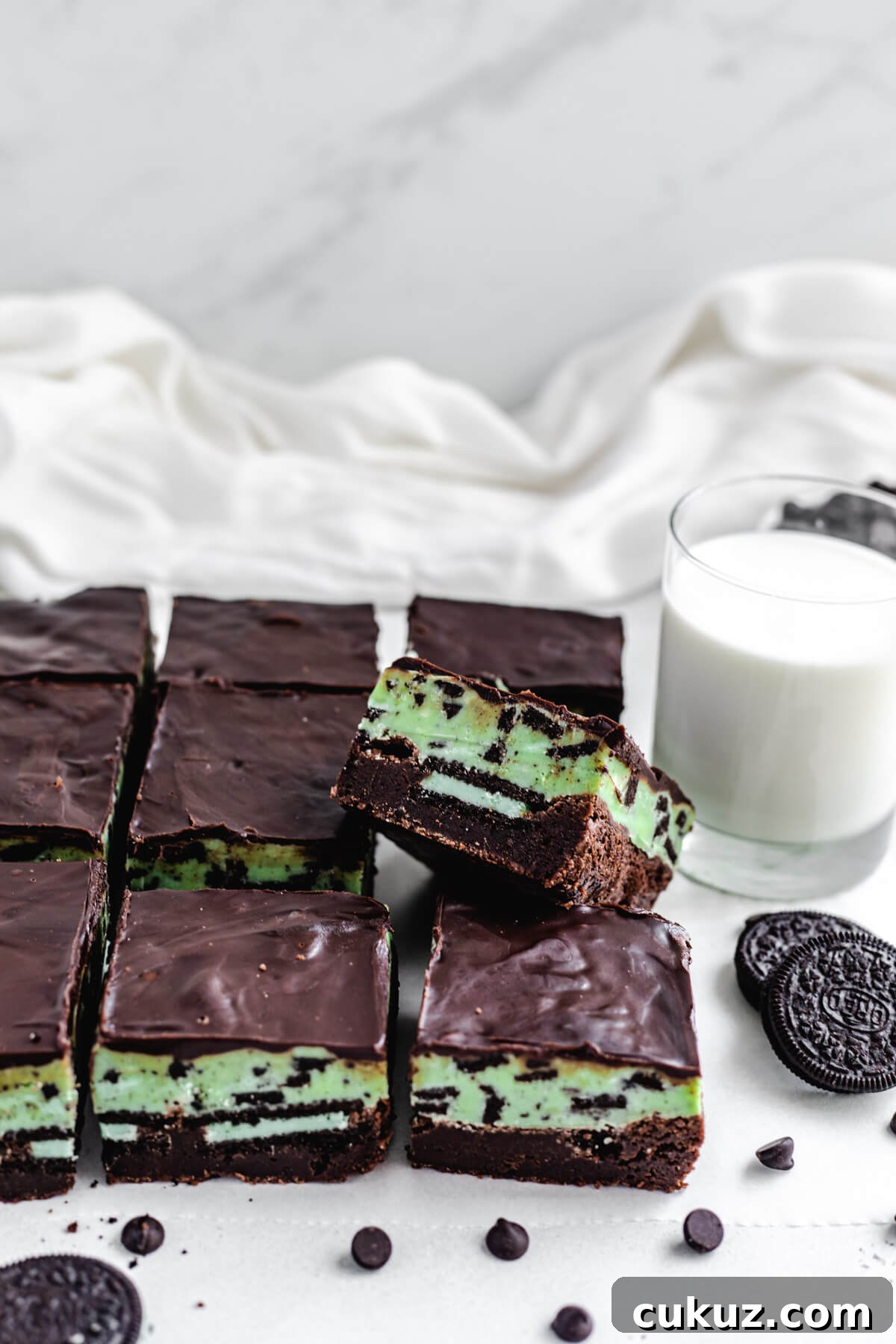brownie leaning on other brownies with glass of milk and Oreos in background