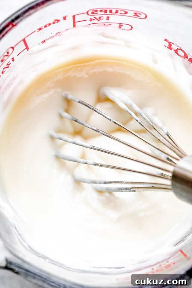 whisking cream cheese frosting in a glass measuring cup