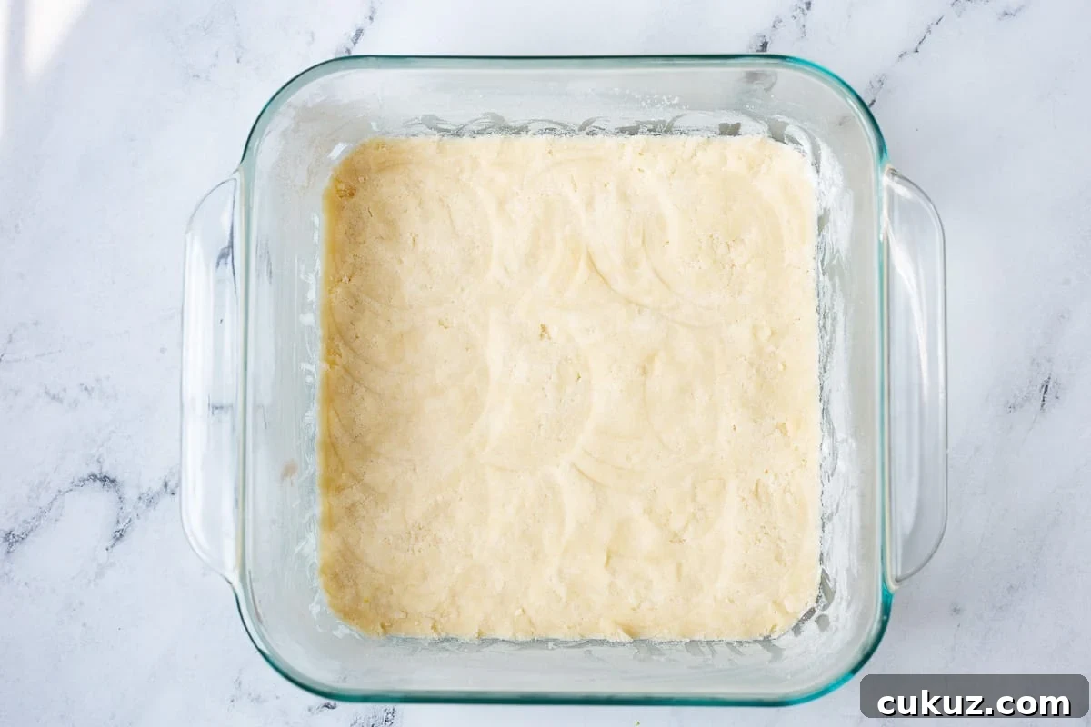 Glass baking dish with shortbread crust pressed into the bottom showing how to make the shortbread crust.