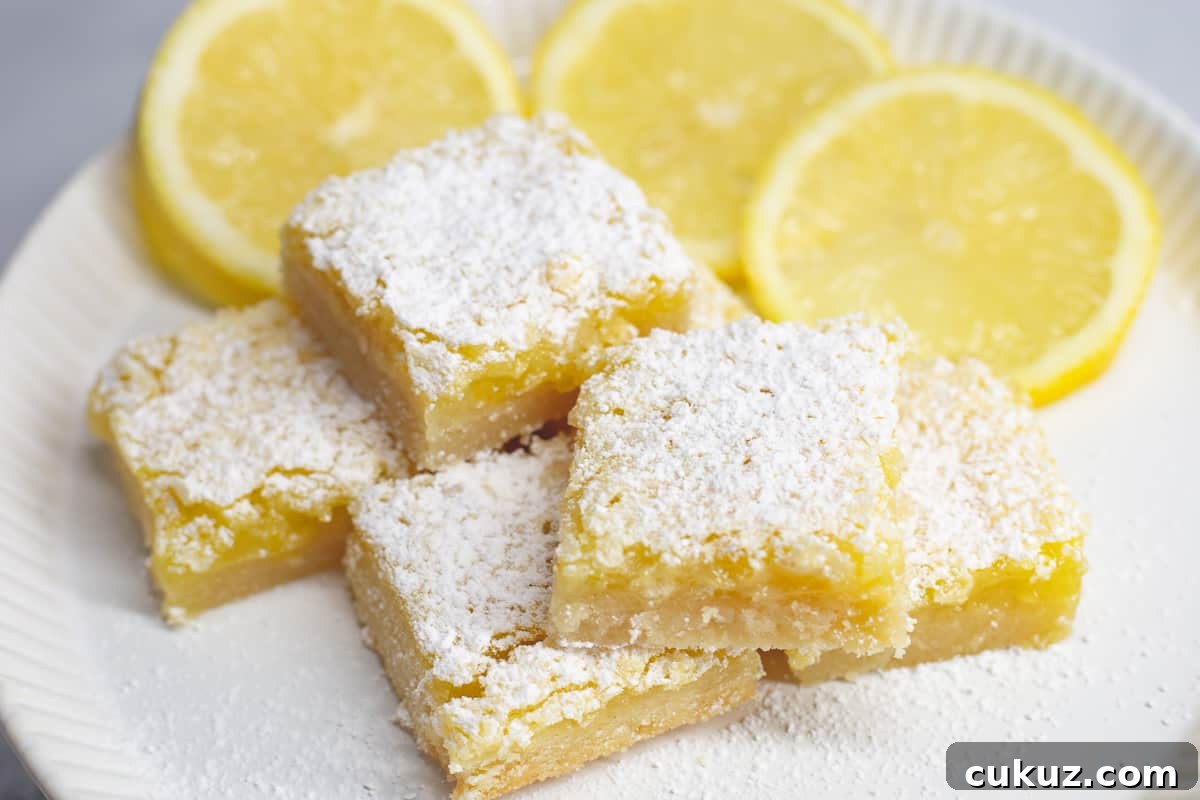 Best ever lemon bar recipe on a white plate with sliced lemons around the bars.