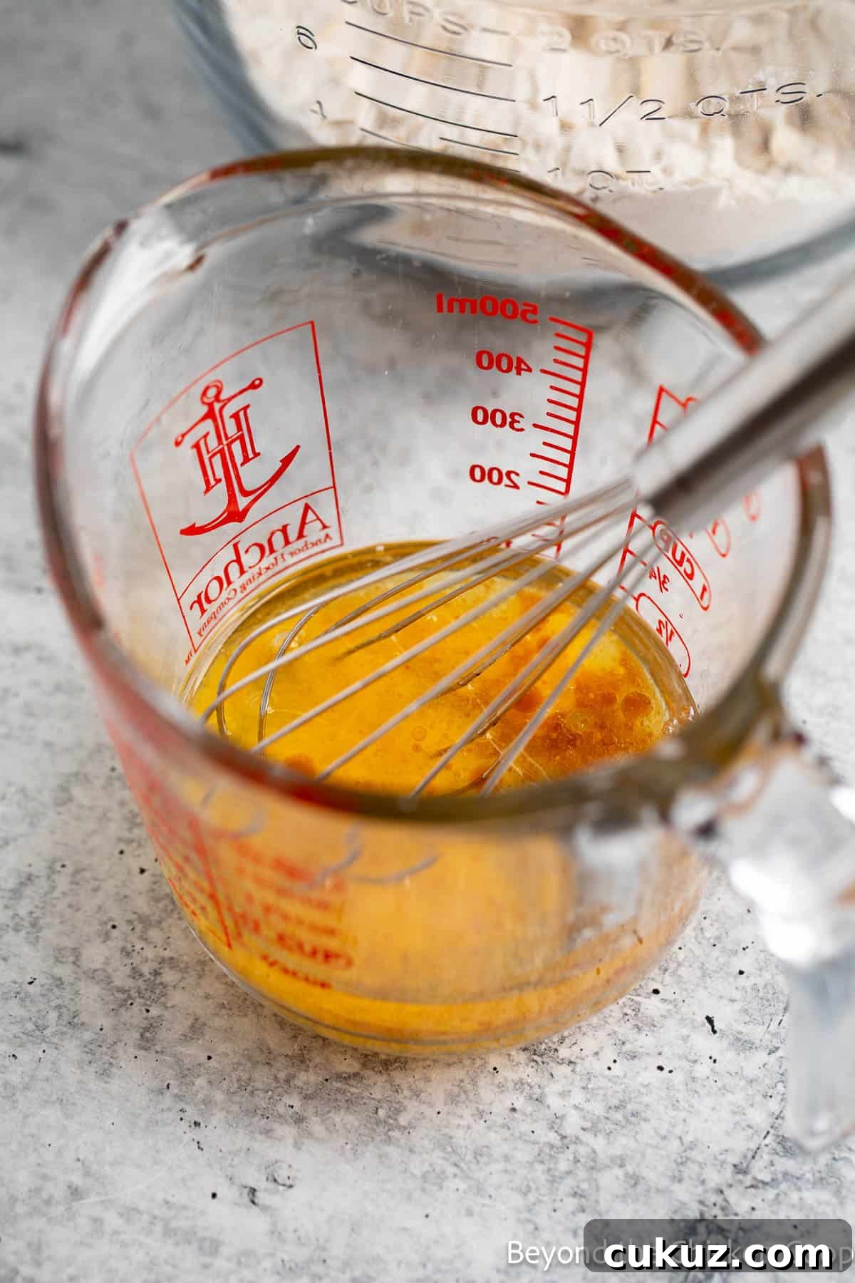 Mixing eggs, oil, and vanilla together in a glass measuring cup with a small whisk. 