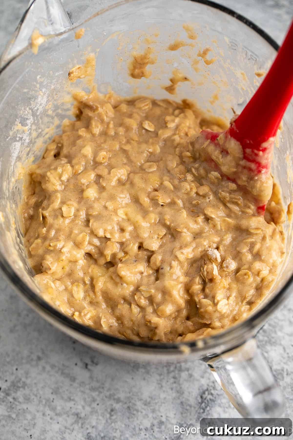 Oat banana batter in a glass bowl with a red spatula. 