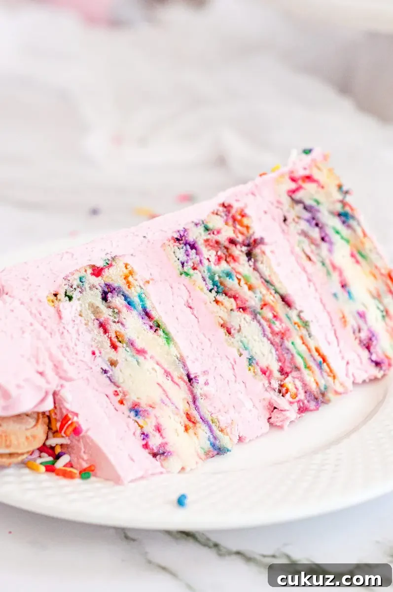 A slice of brightly sprinkled funfetti cake sitting on a white plate. There is pink frosting between each cake layers.