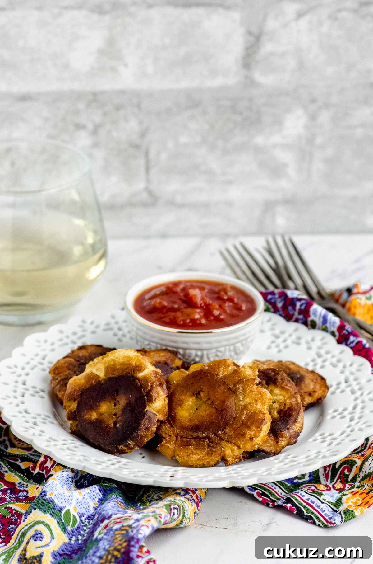 Side view of a white plate with tostones and a small bowl with red salsa on top of a colorful napkin