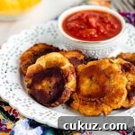 Close-up side view of a white plate with plantains and a small bowl with red salsa