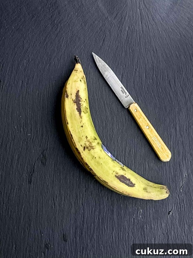 A green plantain on a black surface next to a knife with a yellow handle