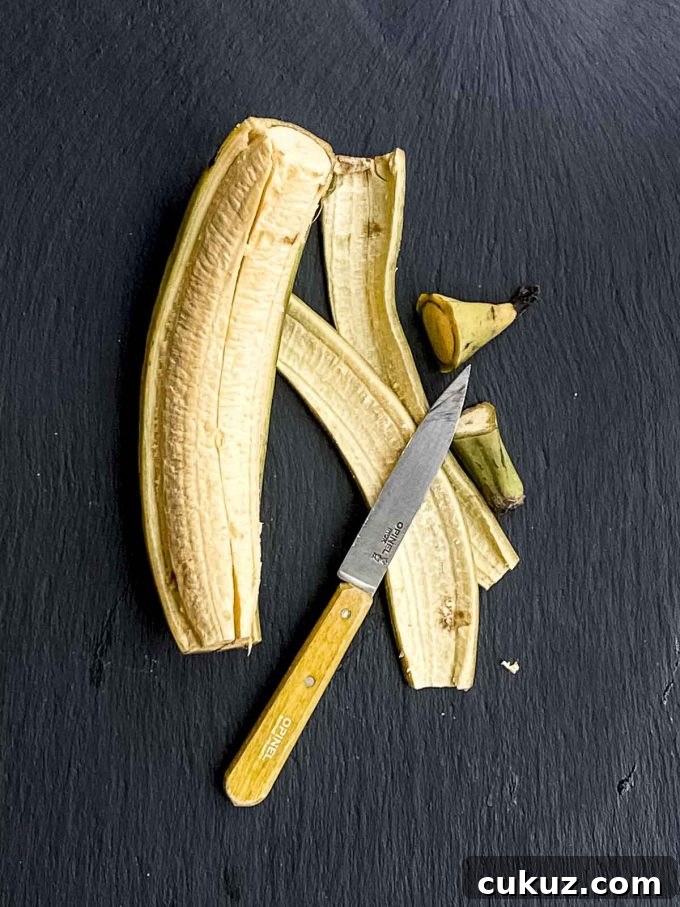 A half peeled plantain on a black surface