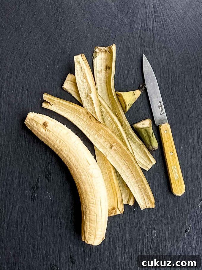 A peel plantain on a black surface next to its peel and a knife with a yellow handle