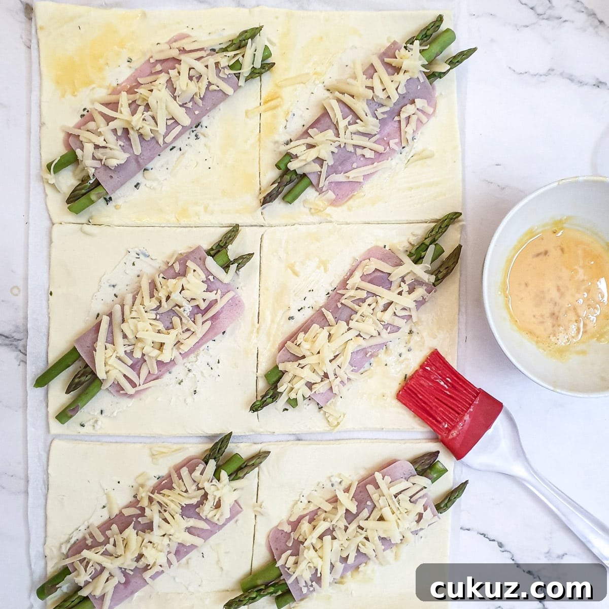 Beaten egg being brushed onto the corners of the ham and asparagus pastry squares.
