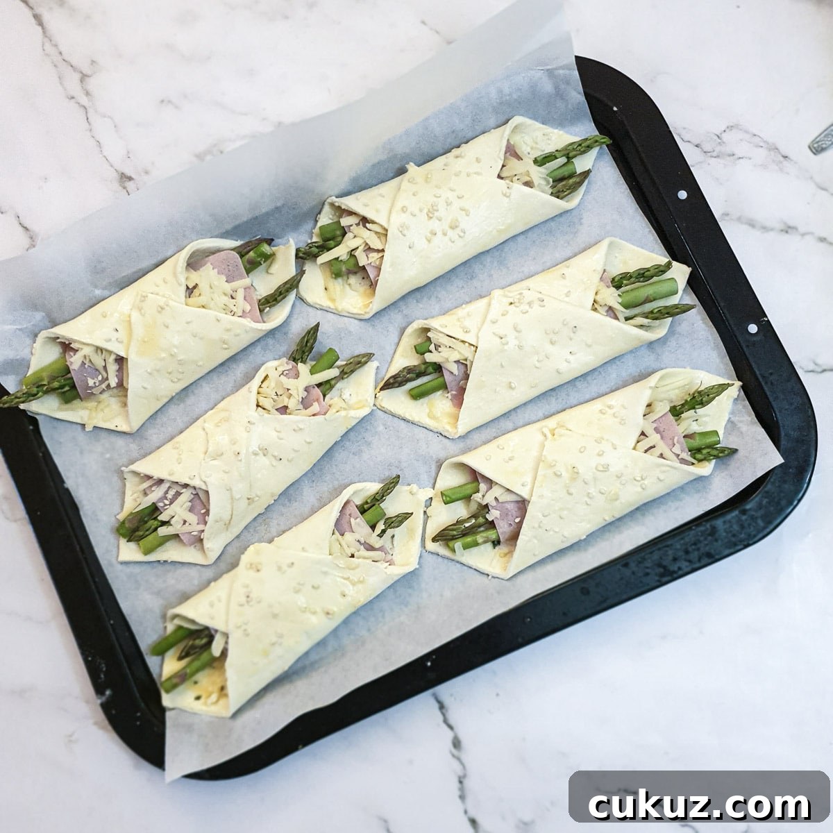 6 puff pastry asparagus and ham wraps on a baking tray.