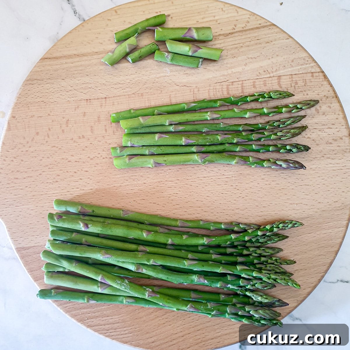 Asparagus spears on a wooden board showing the ends snapped off.